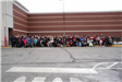 A group of people pose together outside for a picture, they are in front of a red brick building