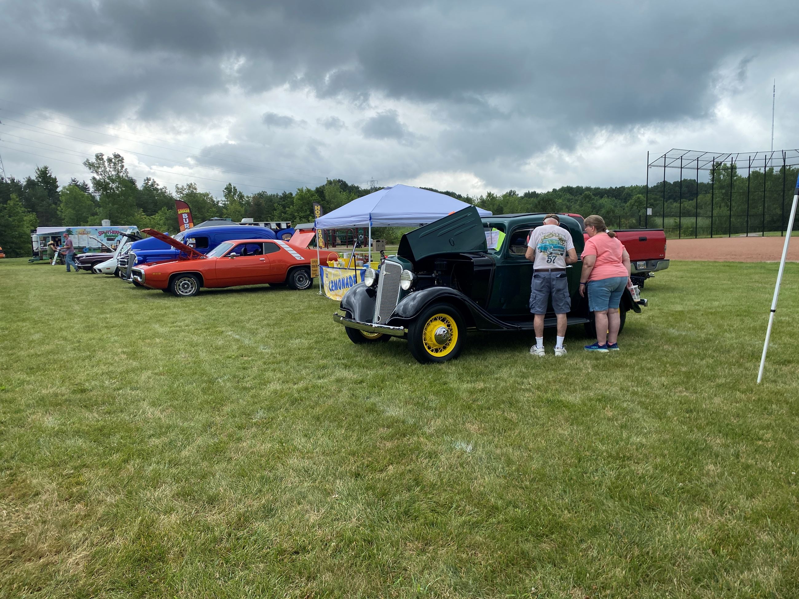Attendees view vintage car, an orange muscle car sits in the background