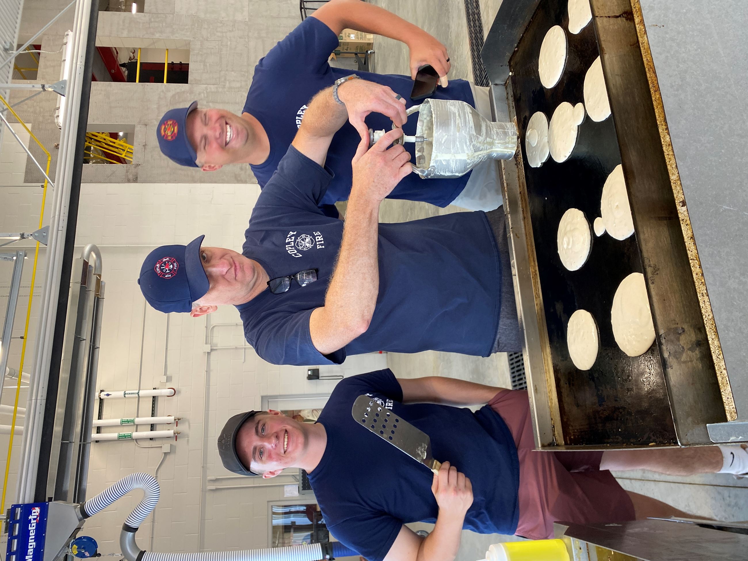 3 Firemen overtop a Griddle making Pancakes at the Copley Safety Center