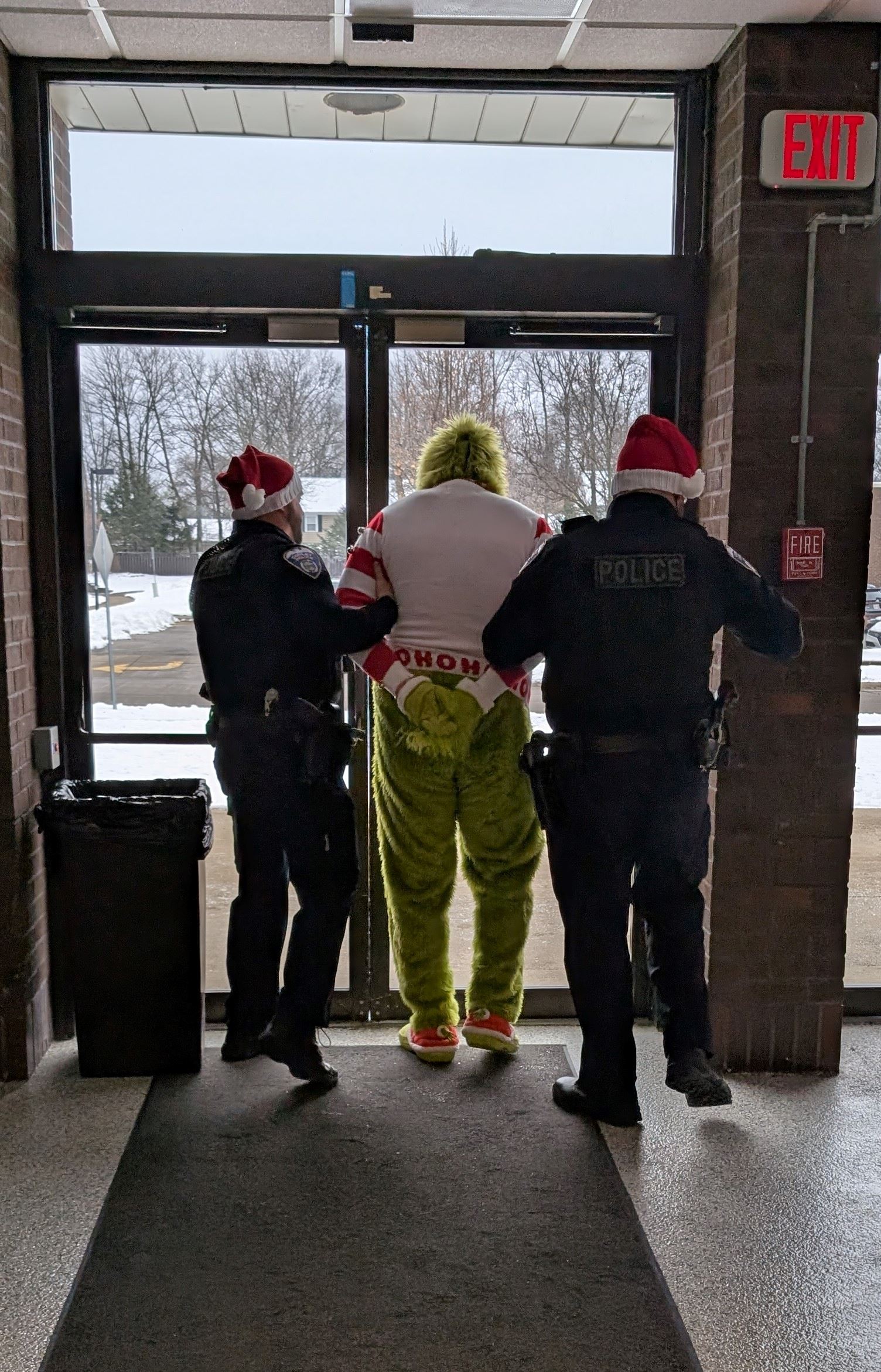 An officer stands on either side of a handcuffed Grinch, walking him to the door