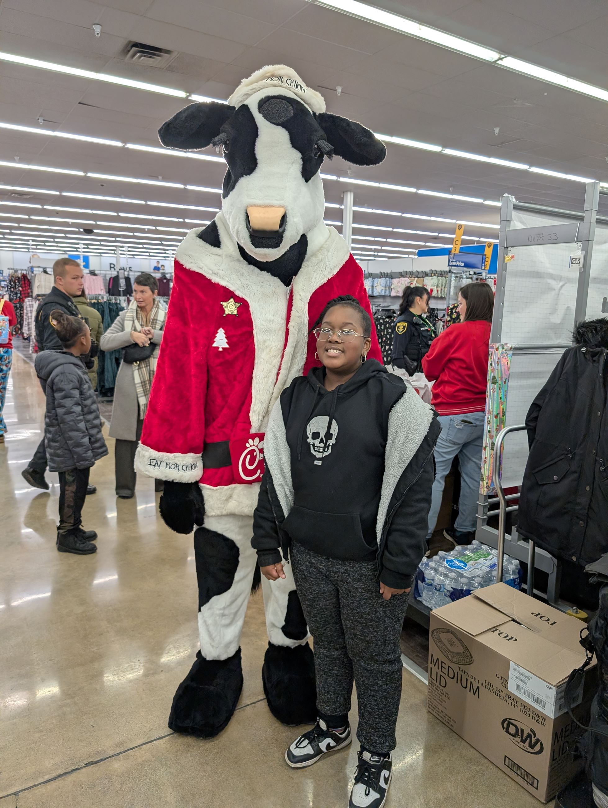 A child stands next to a cow mascot that is wearing a santa suit