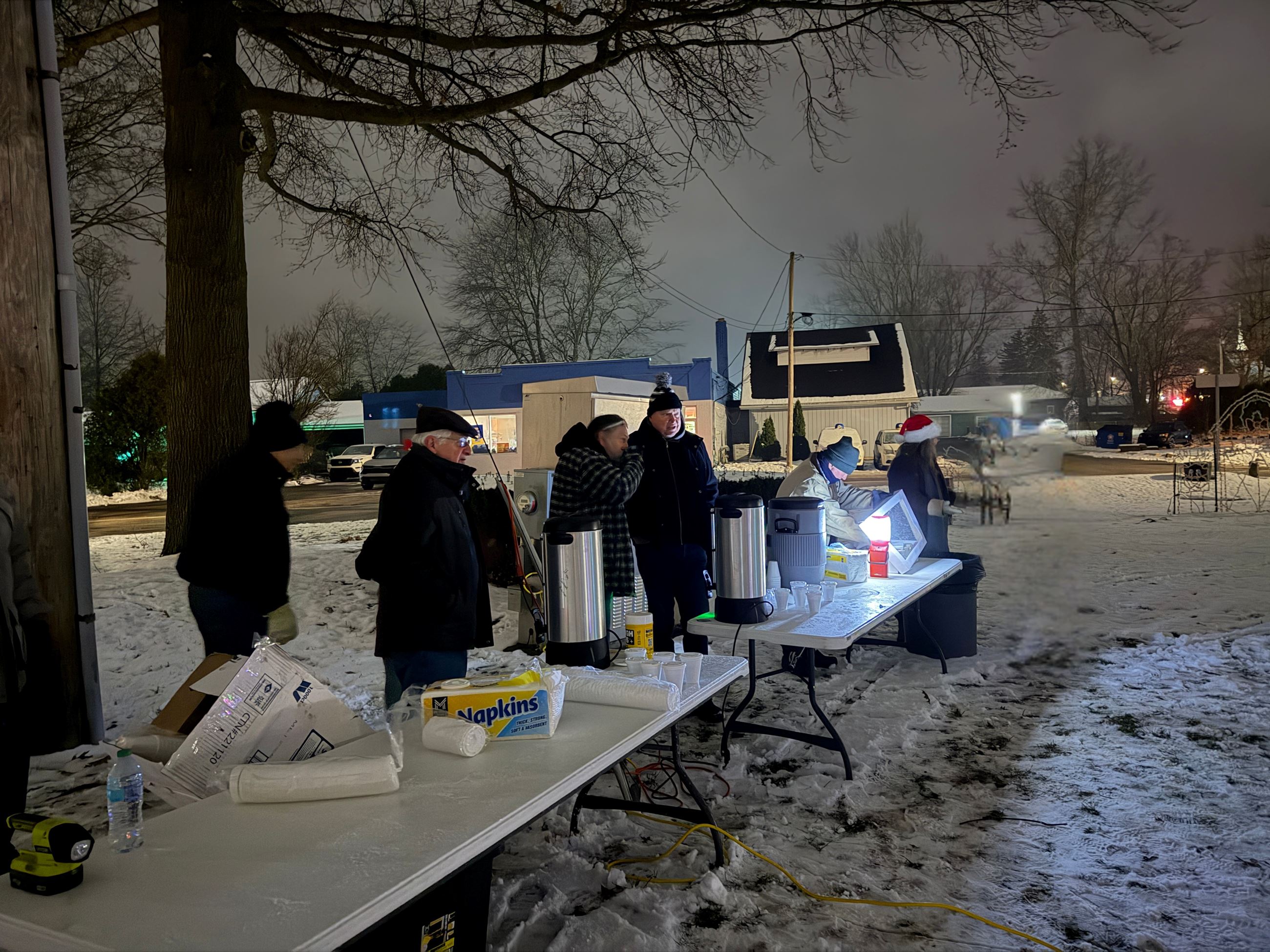 A diverse group of adults working together, behind folding tables outside in the snow