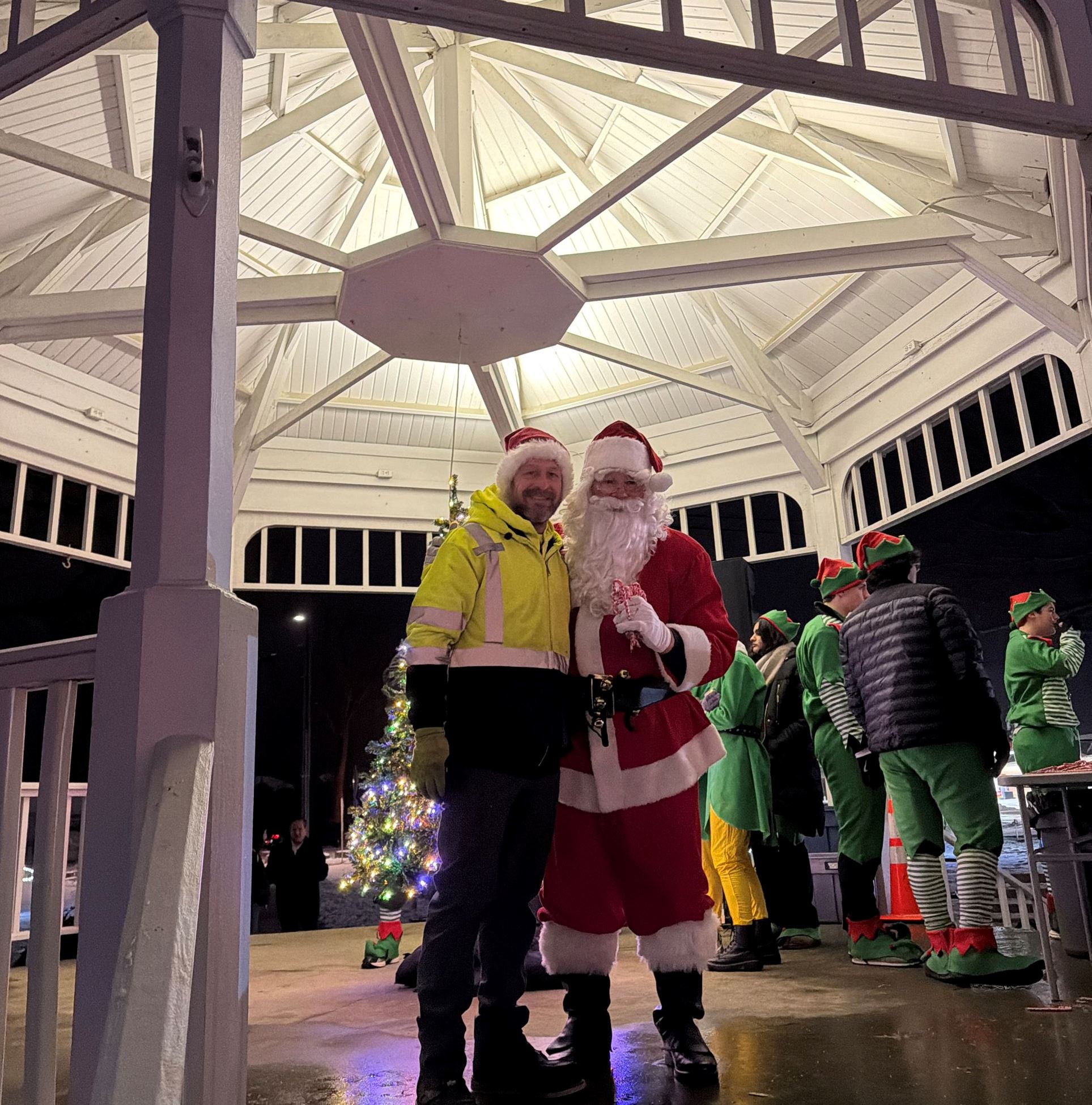A man wearing reflective safety clothing is standing next to santa underneath the Copley Circle Gazebo